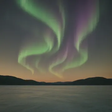 Jigsaw puzzle: Green and purple aurora borealis illuminates the night sky above a frozen lake and distant mountains.