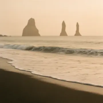 Jigsaw puzzle: A misty morning at a dark sand beach with waves and distant sea stacks.
