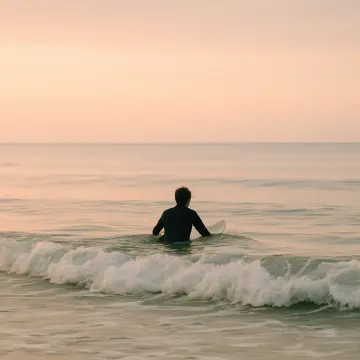 Jigsaw puzzle: A surfer in a wetsuit sits on a surfboard in calm ocean water at dawn.